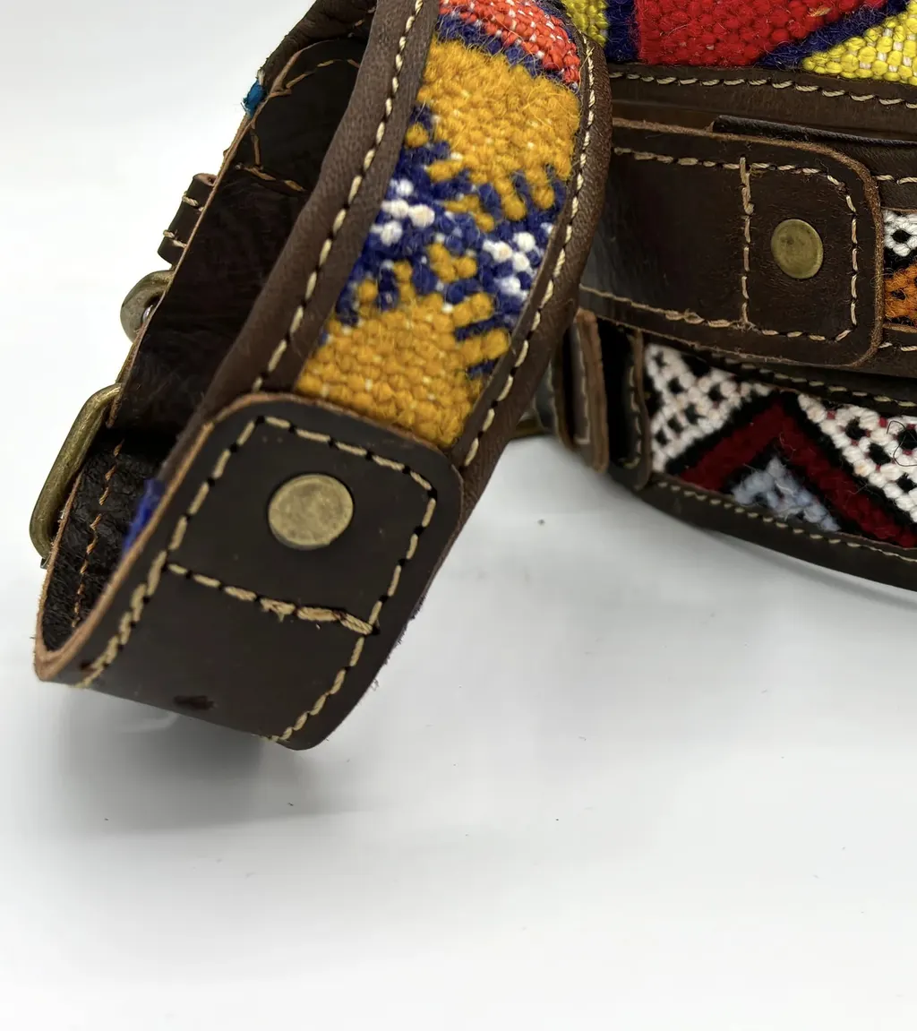 A BohoBarks collar leaning against a stack, showing its stitched edge, rivet and woven saffron band